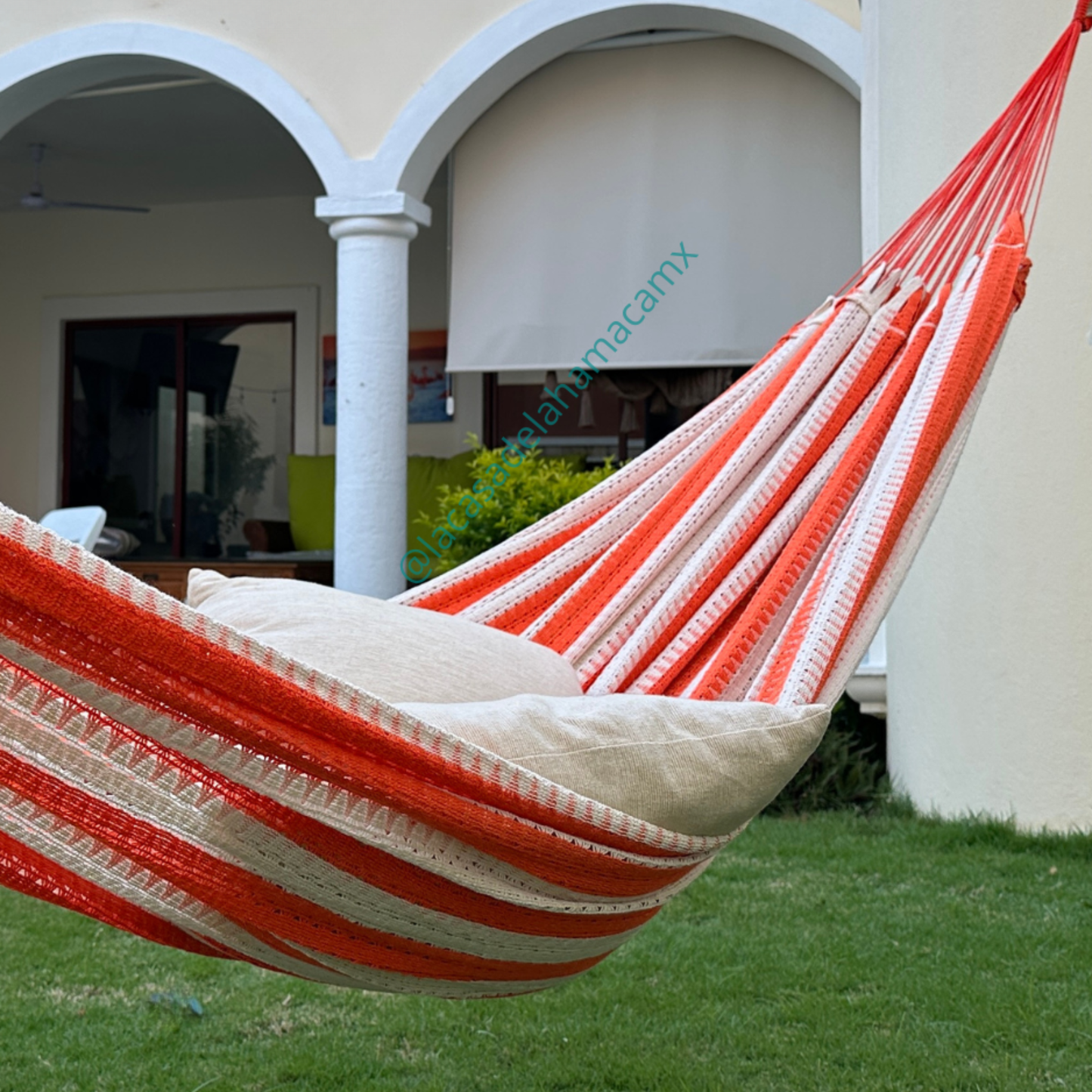 Hamaca naranja grande de algodón colgada en jardín de casa, con dos cojines
