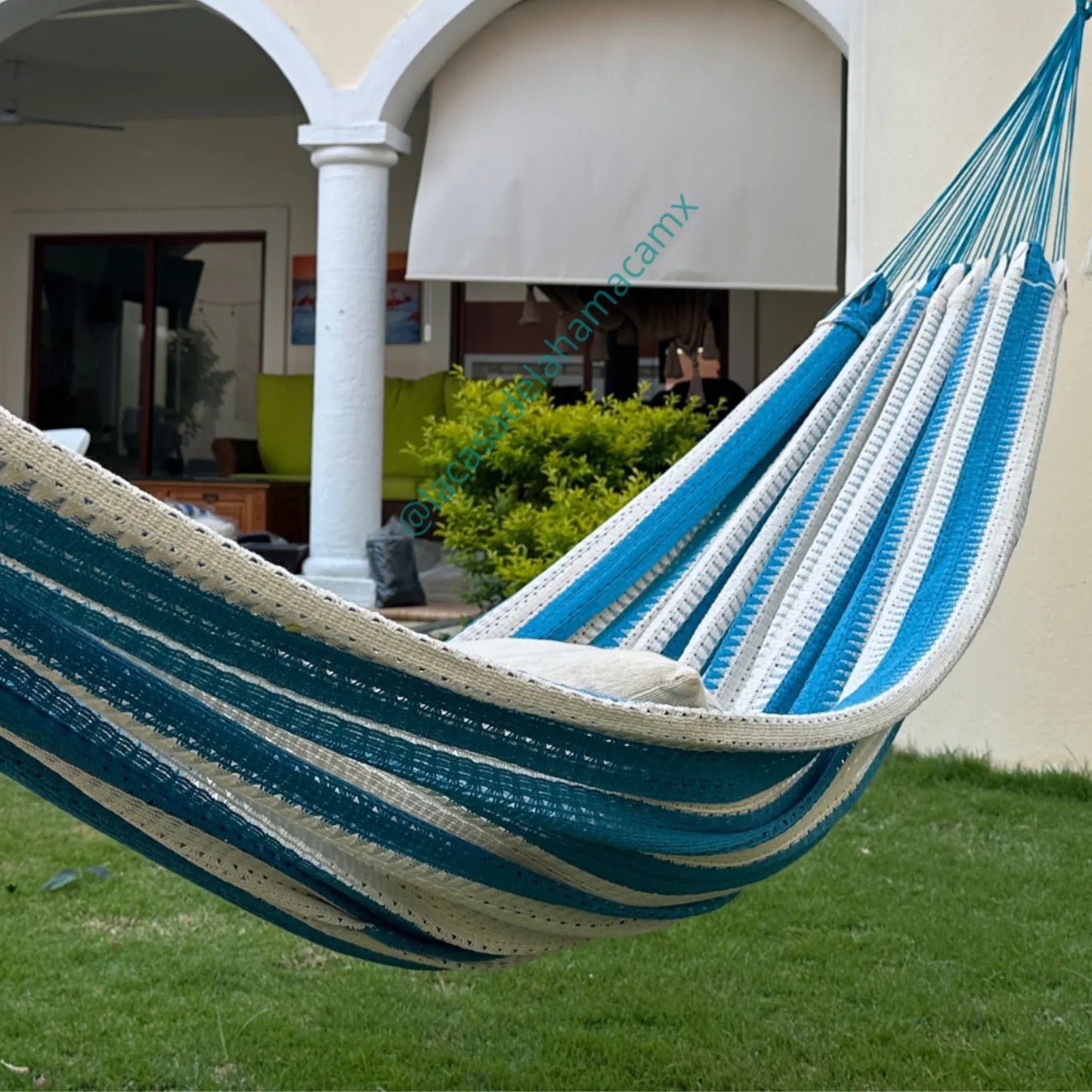 Hamaca turquesa y beige grande de algodón colocada en jardín de casa
