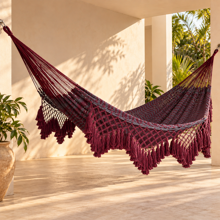 Hamaca yucateca artesanal de algodón rojo y gris con macramé colgada en una terraza con plantas tropicales