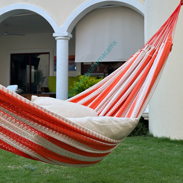 Hamaca naranja grande de algodón colgada en jardín de casa, con dos cojines