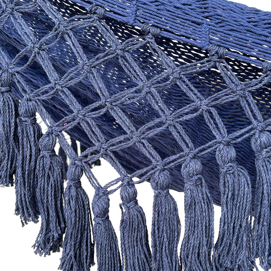 Primer plano del macramé azul con nudos en forma de rombos y flecos decorativos en el borde de una hamaca artesanal de algodón.