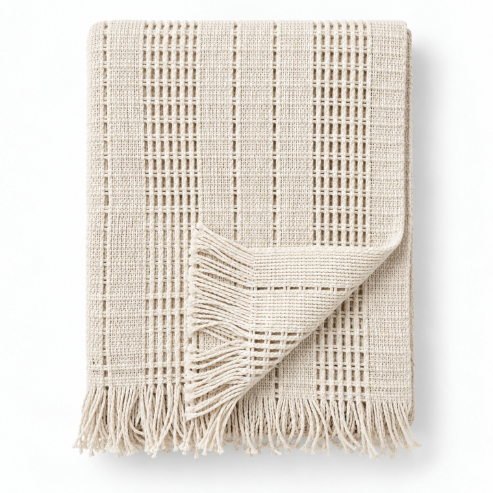 Manta mexicana de algodón KENUF color beige, doblada sobre fondo claro, mostrando su tejido y flecos decorativos.